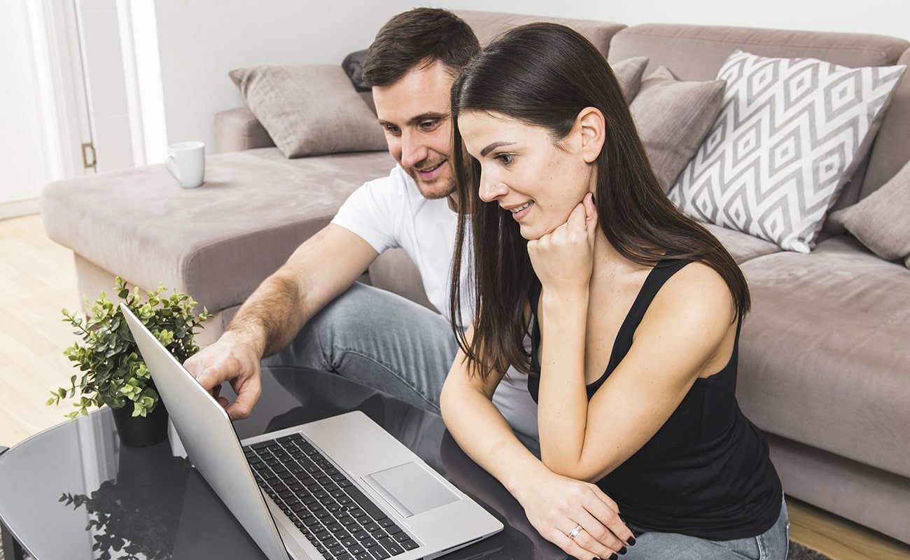 smiling-young-couple-using-laptop-home-min